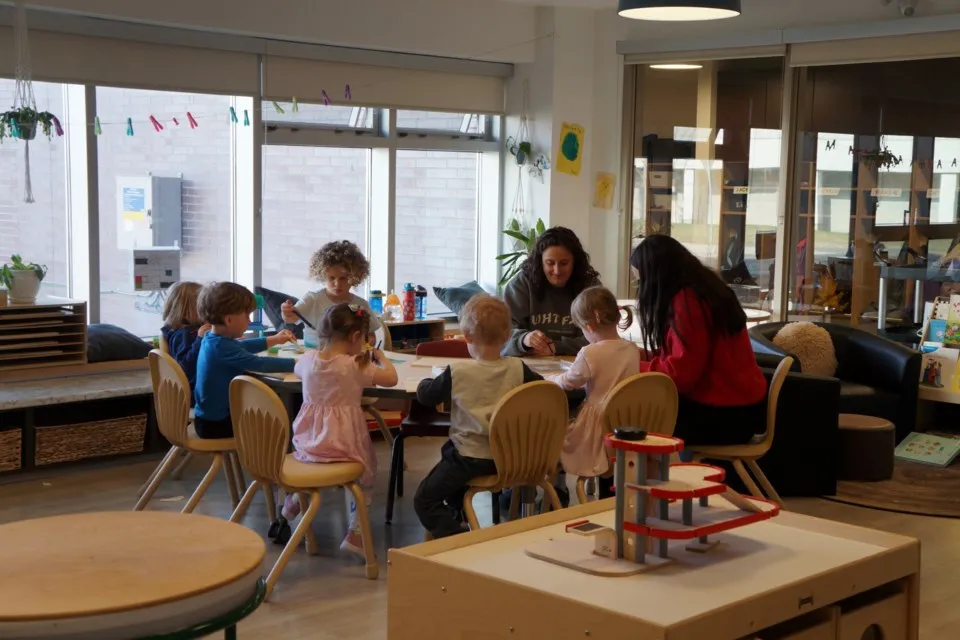Members of the Laurentian Child and Family Centre team sit at a table doing crafts with a group of small children.
